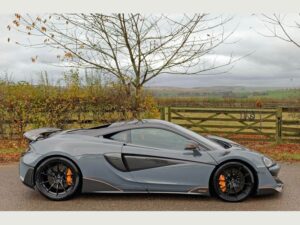 Side profile of a grey McLaren 600LT parked beside a wooden gate