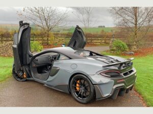 Grey McLaren 600LT with both doors raised, viewed from the rear three-quarter angle